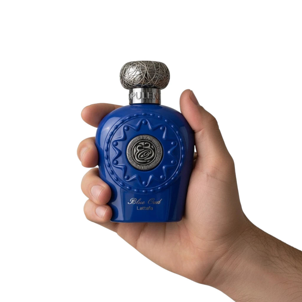 Hand holding a Lattafa Blue Oud perfume bottle with intricate design on a white background