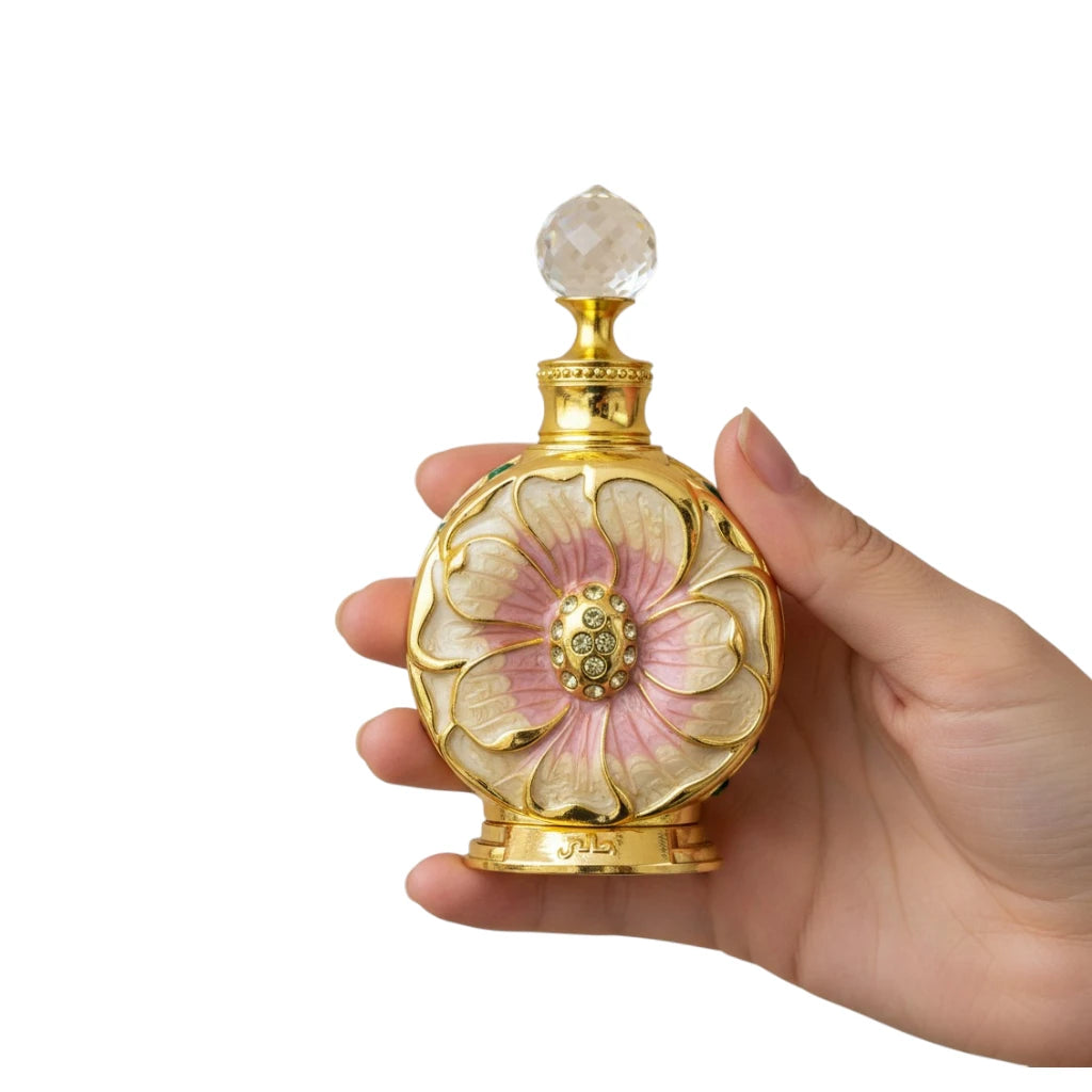 Hand holding a Amaali Perfume Oil bottle with floral design and gold accents on a white background