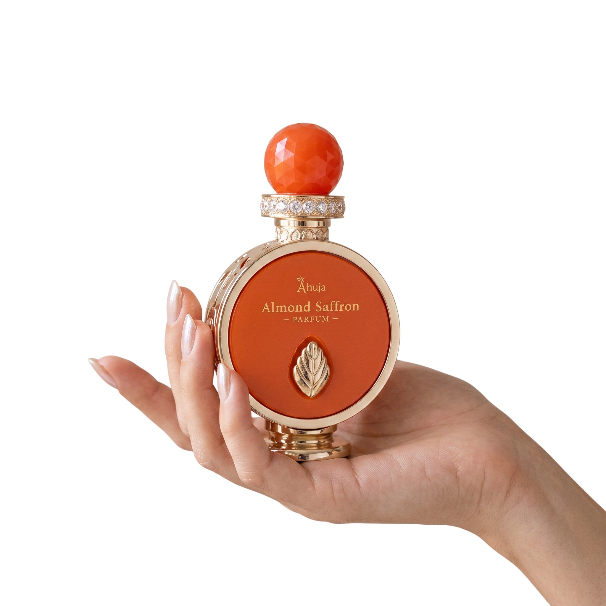 Palette 21 Ahuja Almond Saffron parfum bottle with orange glass, gold accents, and crystal cap held in a hand.