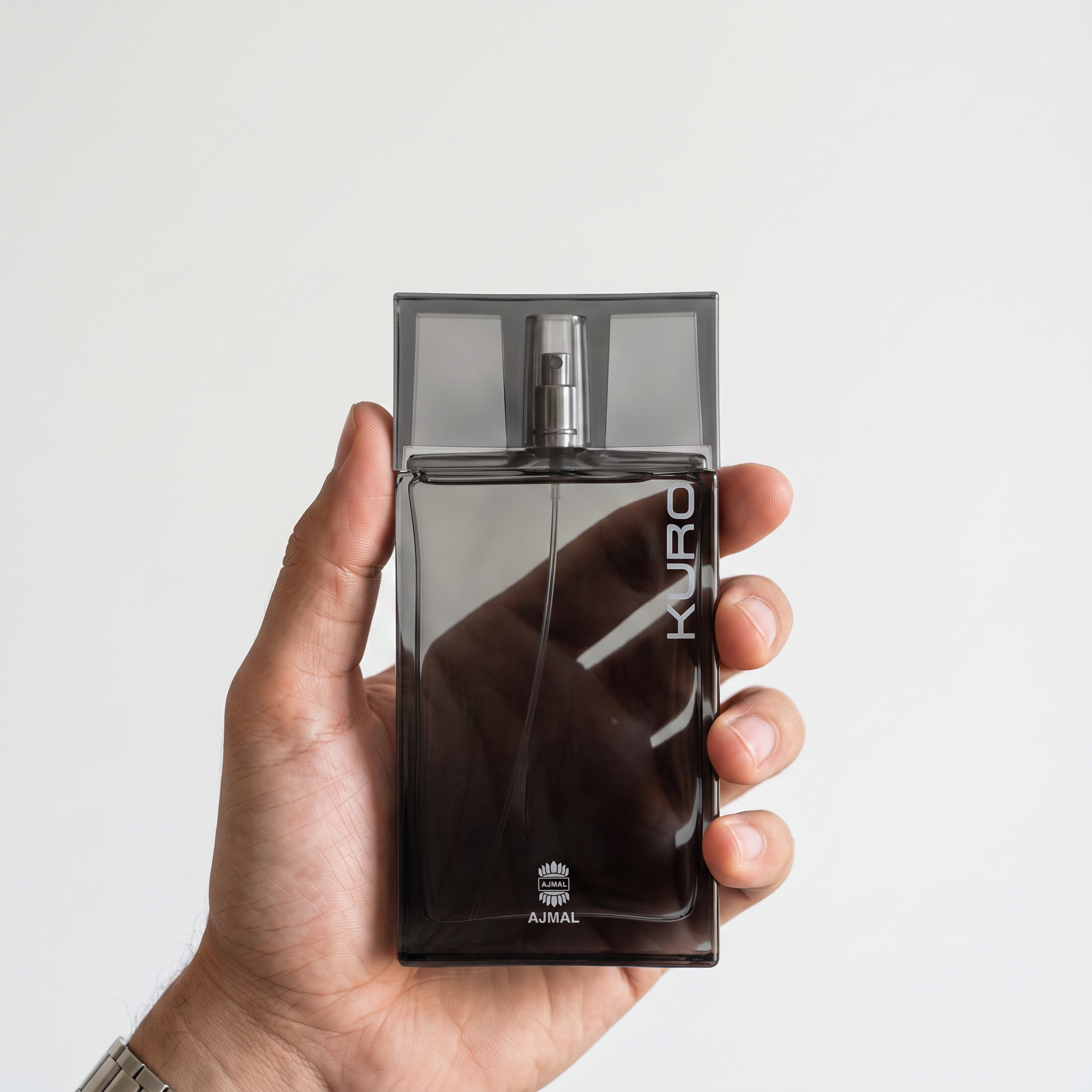 Palette 21 AJMAL Kuro Eau de Parfum in a sleek, dark grey glass bottle held in a hand against a white background.