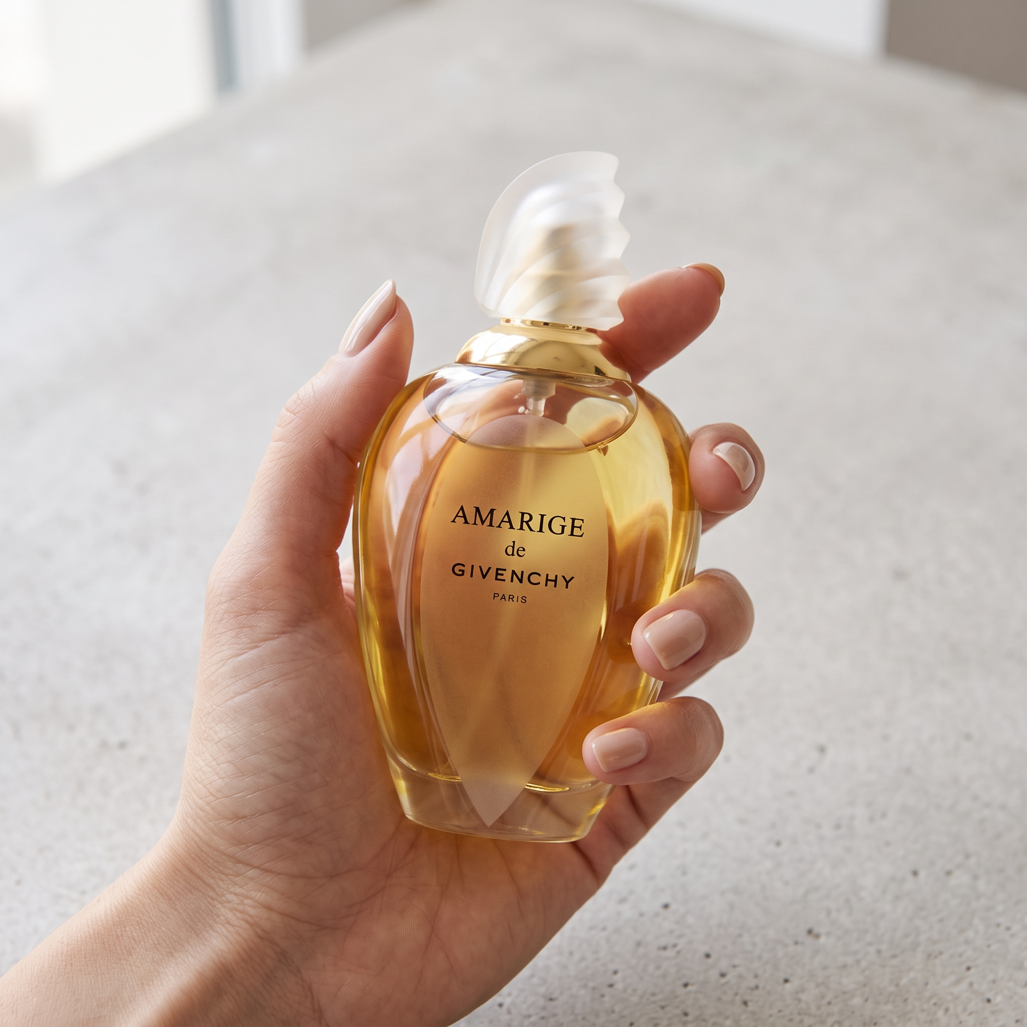Palette 21 Amarige de GIVENCHY Eau de Toilette spray bottle held in a hand against a neutral stone background.