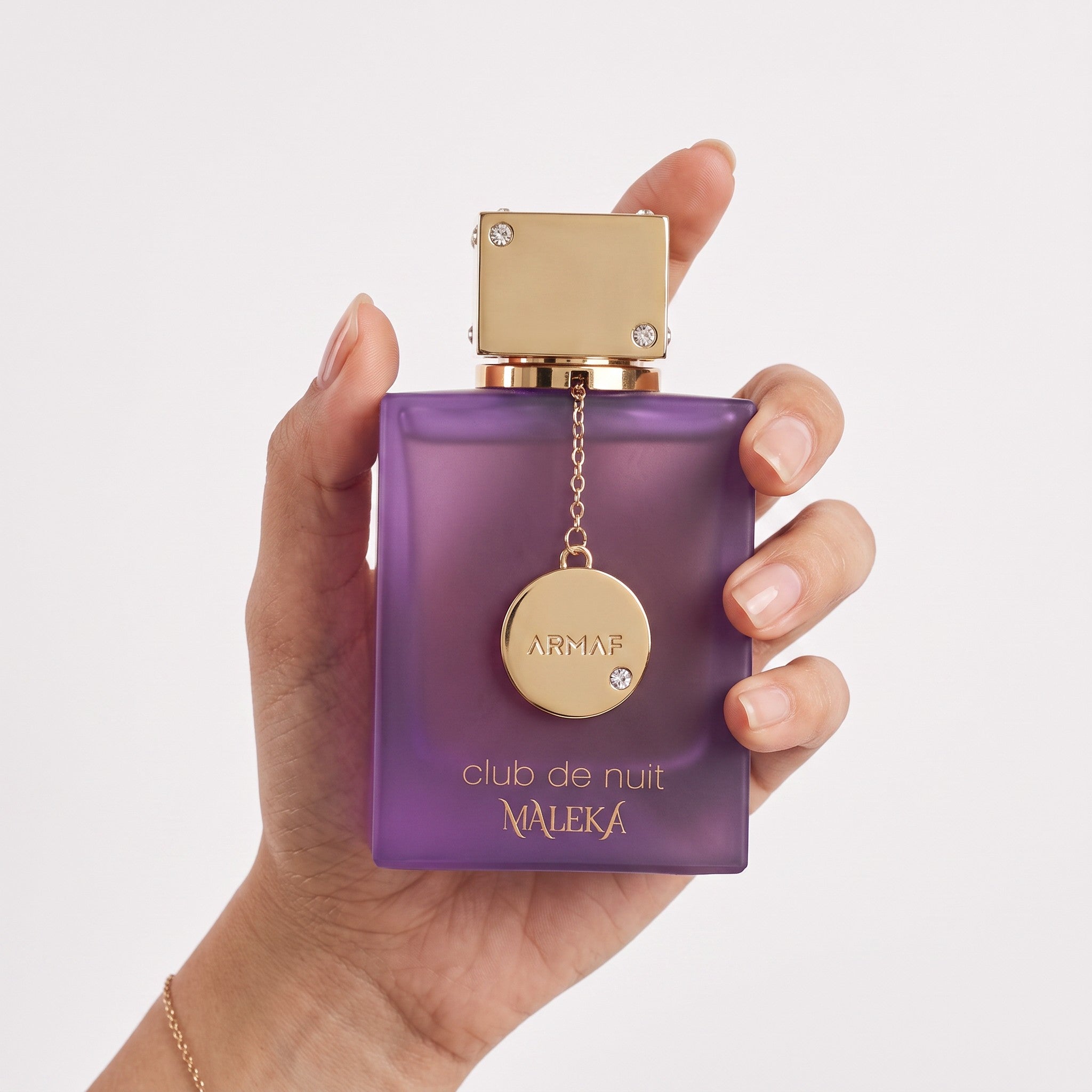 Palette 21 Armaf Club De Nuit Maleka perfume in a purple glass bottle with gold charm held in a woman's hand