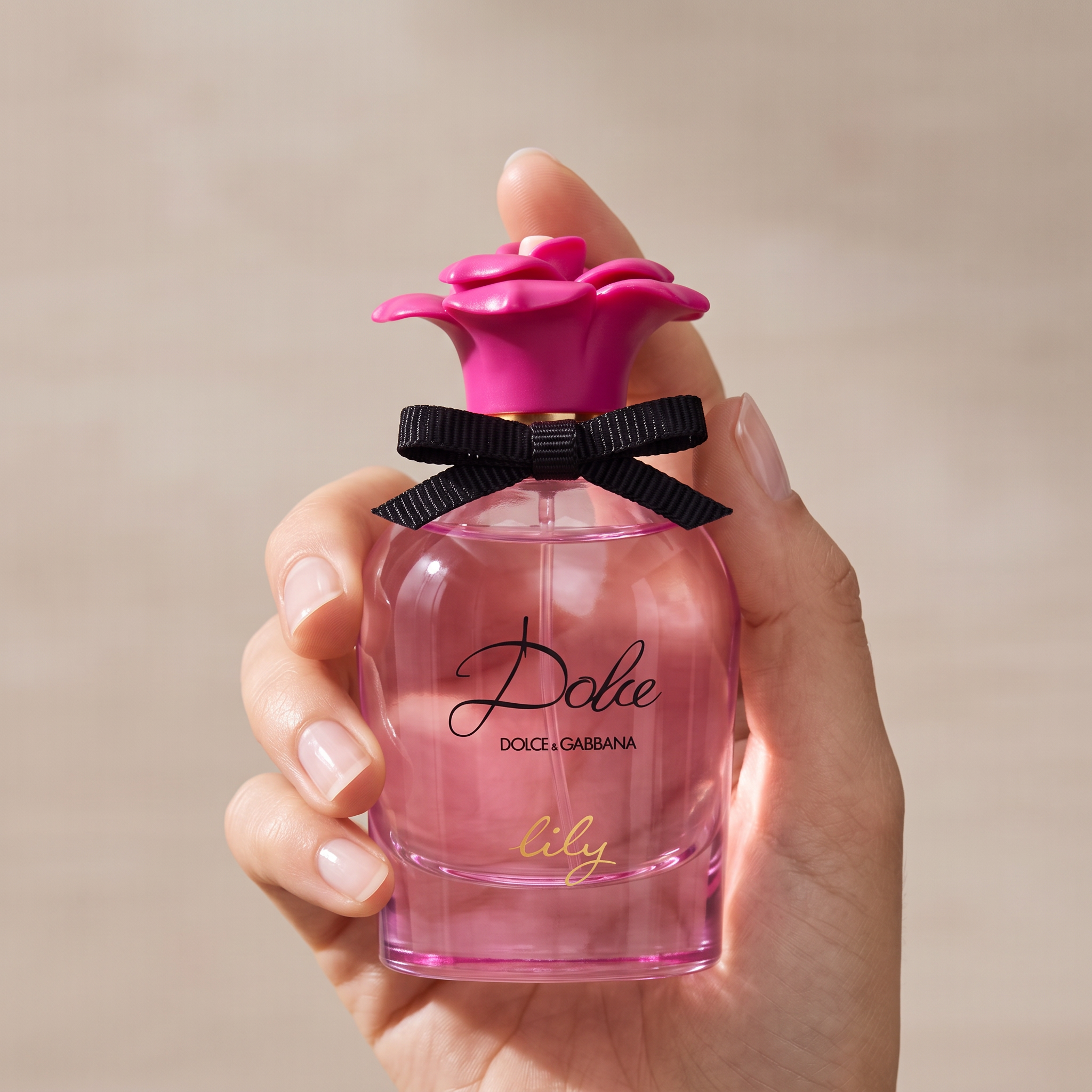 Palette 21 Dolce & Gabbana Dolce Lily perfume bottle with pink liquid, floral cap, and black ribbon held in a hand