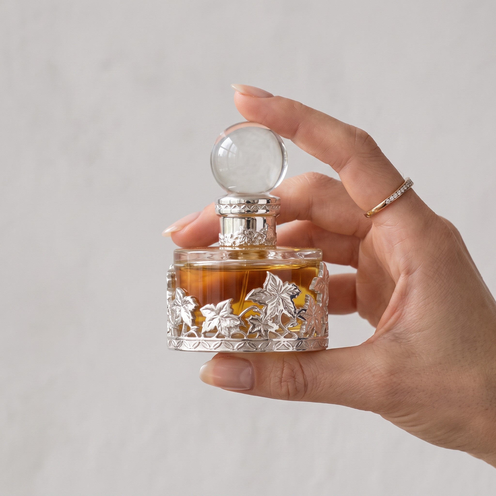 Palette 21 SWISS ARABIAN Rose Malaki perfume oil in an ornate silver-toned glass bottle held by a woman's hand.