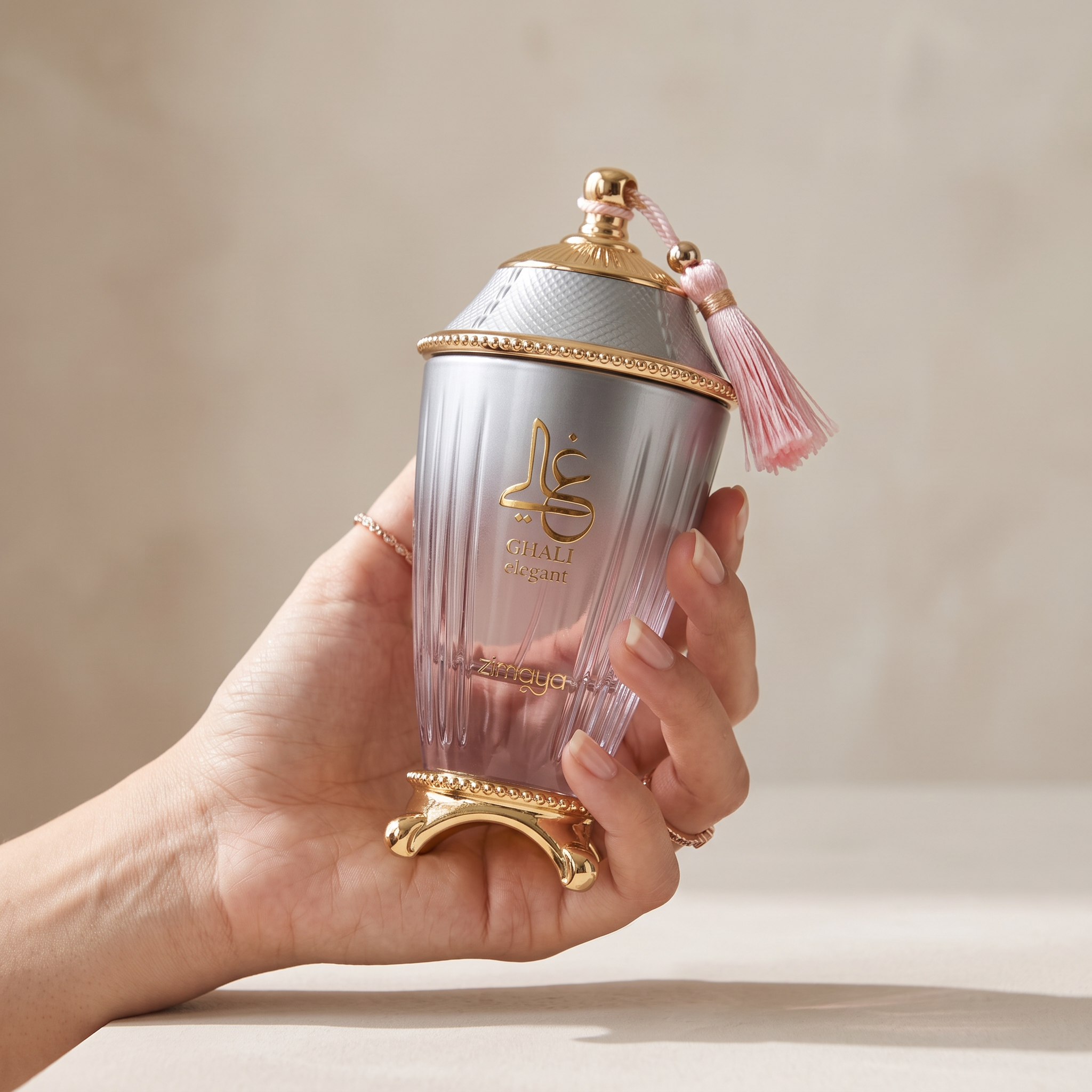 Palette 21 Zimaya Ghali Elegant perfume bottle with a gradient finish, gold accents, and a pink tassel held in a hand.